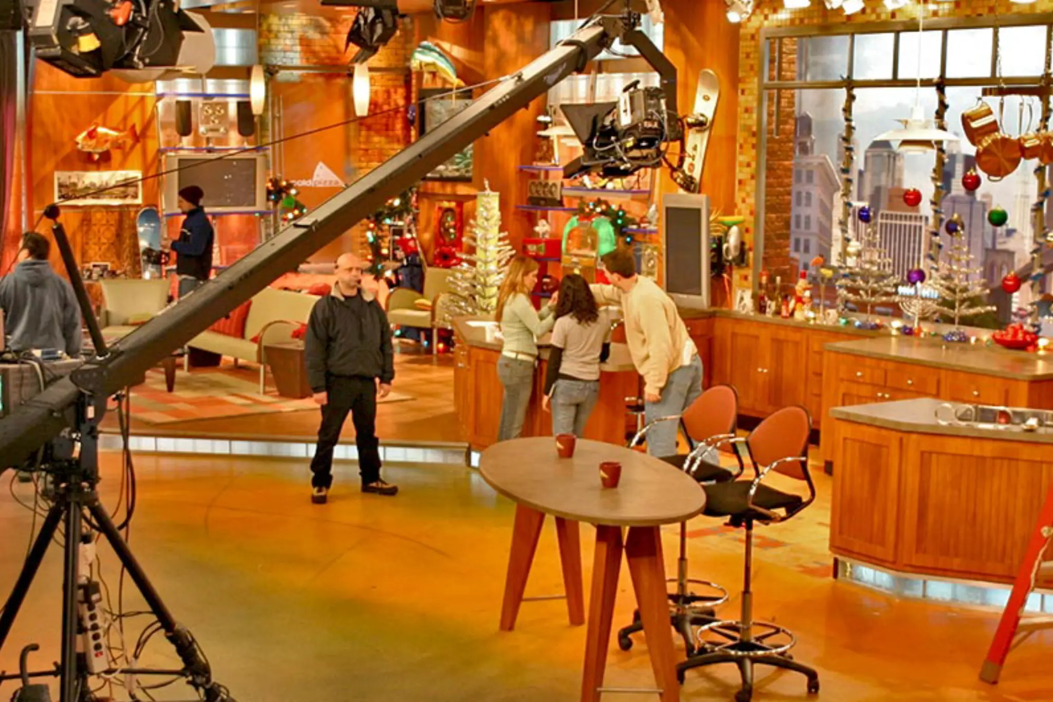 A brightly lit television studio with a large crane camera, wooden set pieces, and festive decorations, preparing for a show