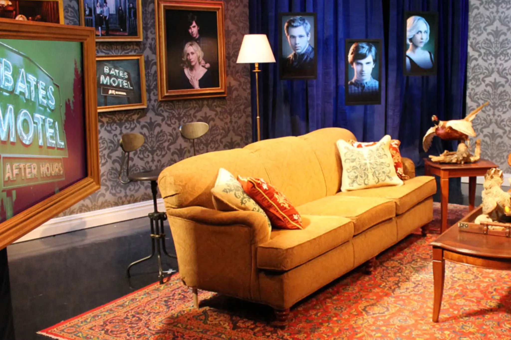 Cozy set from _Bates Motel_ featuring a mustard-colored couch, decorative pillows, a wooden coffee table, and vintage decor on the walls Cozy set from _Bates Motel_ featuring a mustard-colored couch, decorative pillows, a wooden coffee table, and vintage decor on the walls