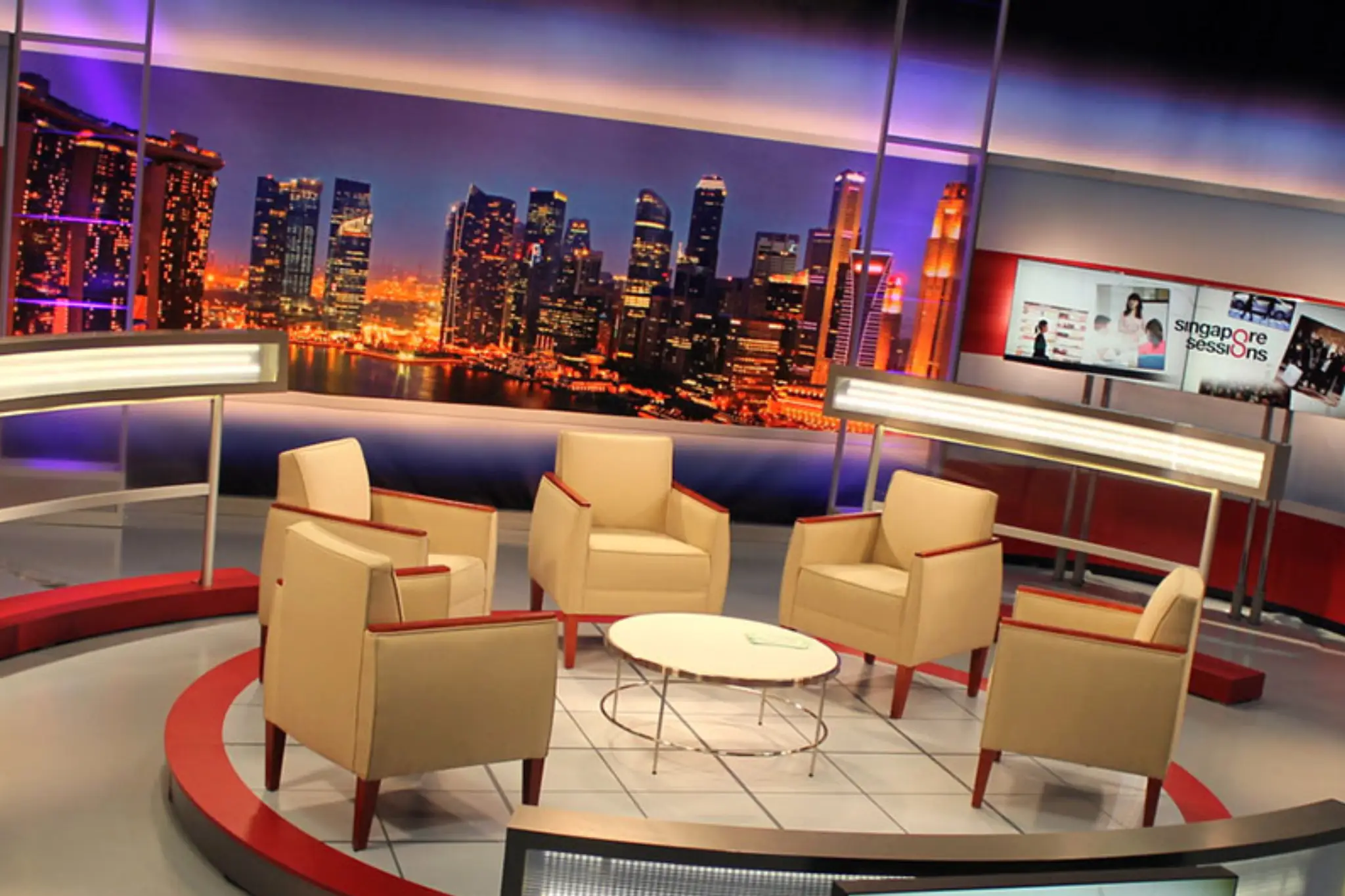 Modern TV studio set with beige chairs and a round table, featuring a vibrant city skyline backdrop and _Singapore Sessions_ display