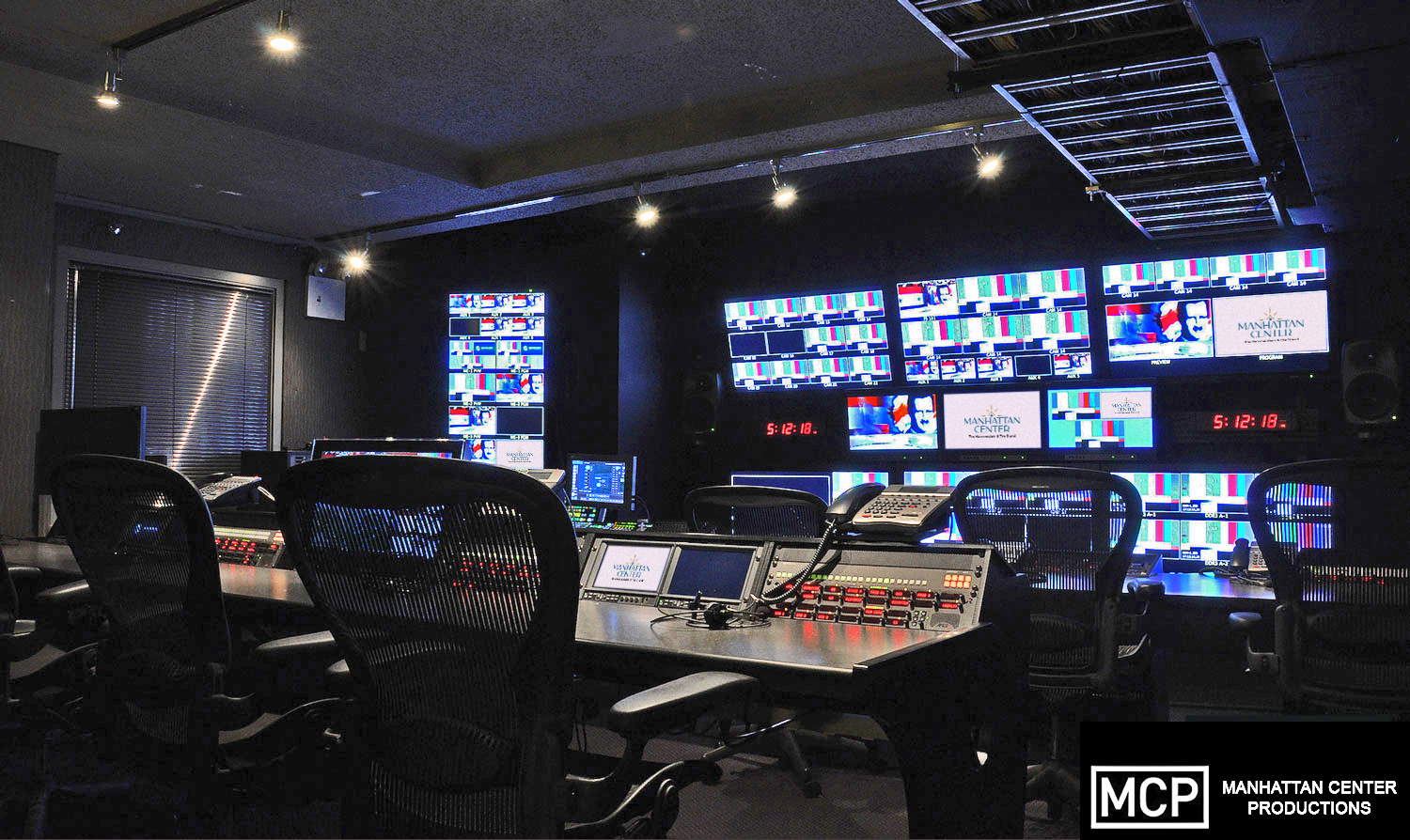 19fbc97b4d9e4014b4f32485e029822a A modern audio control room featuring a large mixing console, multiple screens, sound equipment, and a swivel chair
