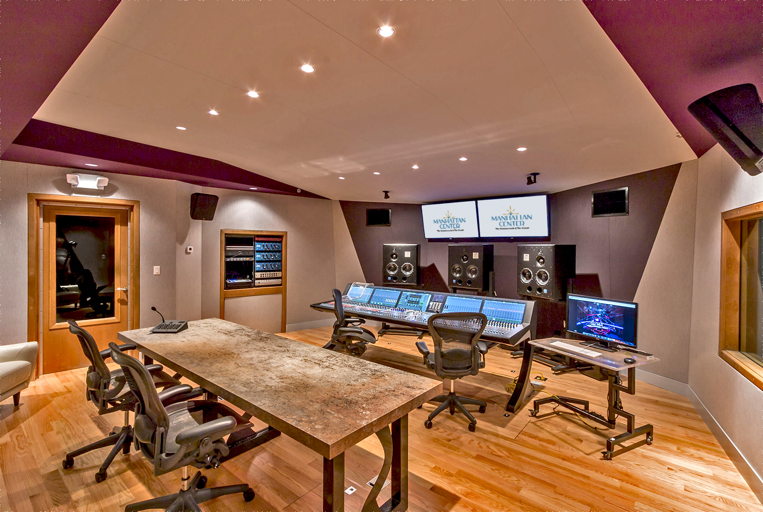 mc audio studio 7 lrg 2025-logo (2) A modern music studio featuring a large mixing console, multiple audio monitors, and screens displaying sound levels